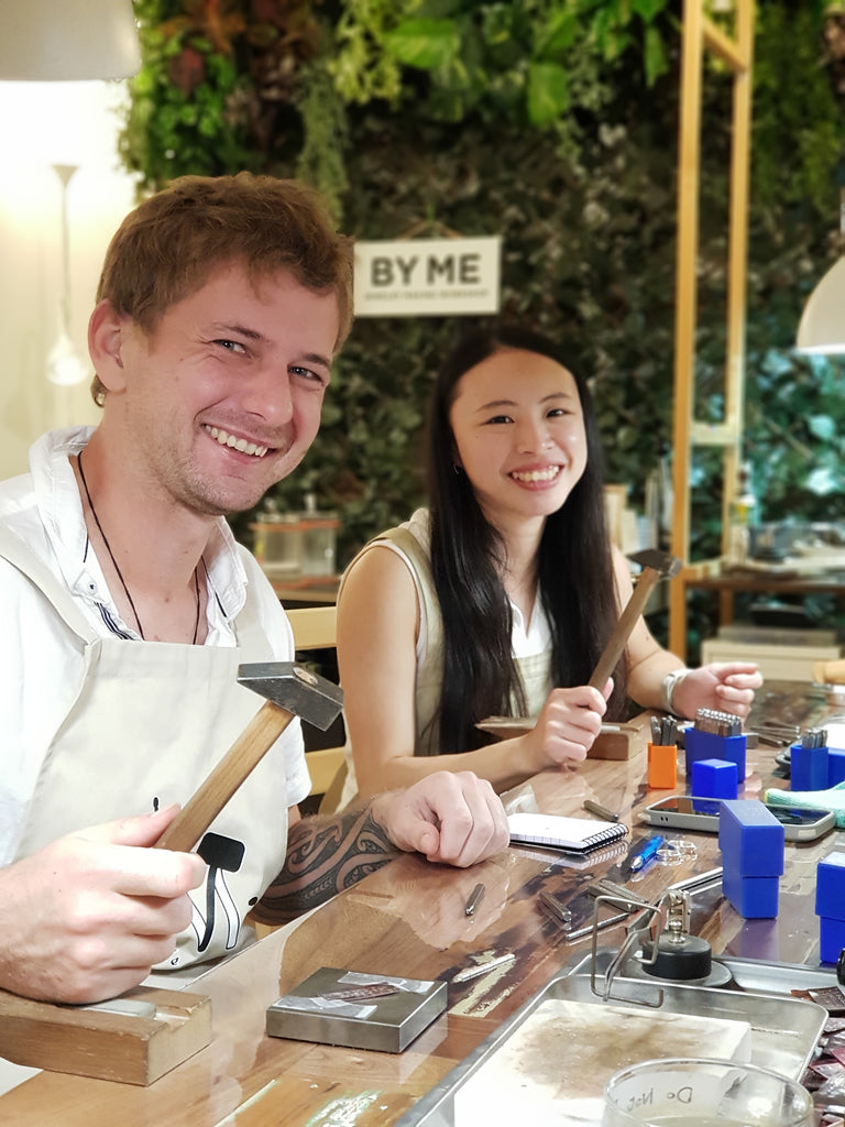 Happy Couple with hammers and stamping pins while practicing hand stamping  during their Couple Ring-Making Class at enchanted Jewellery-Making Workshop: ByMe Workshop, Brisbane.
